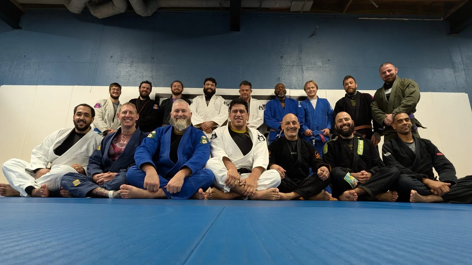Group of adult Brazilian Jiu Jitsu students and instructors in mixed-color gis gathered for a class photo.
