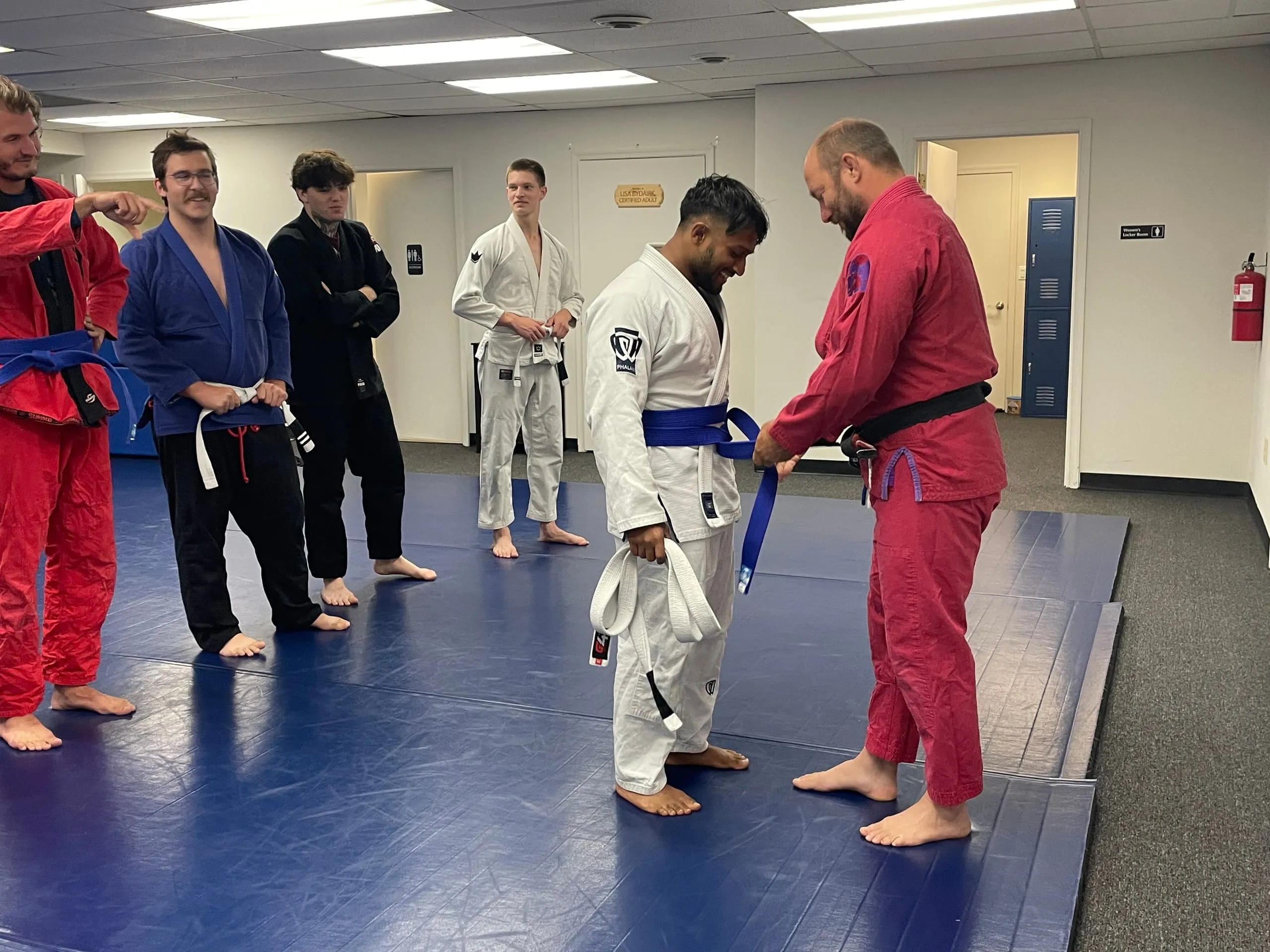 Eric Bydairk ties a newly earned blue belt on a student during a jiu jitsu promotion ceremony.