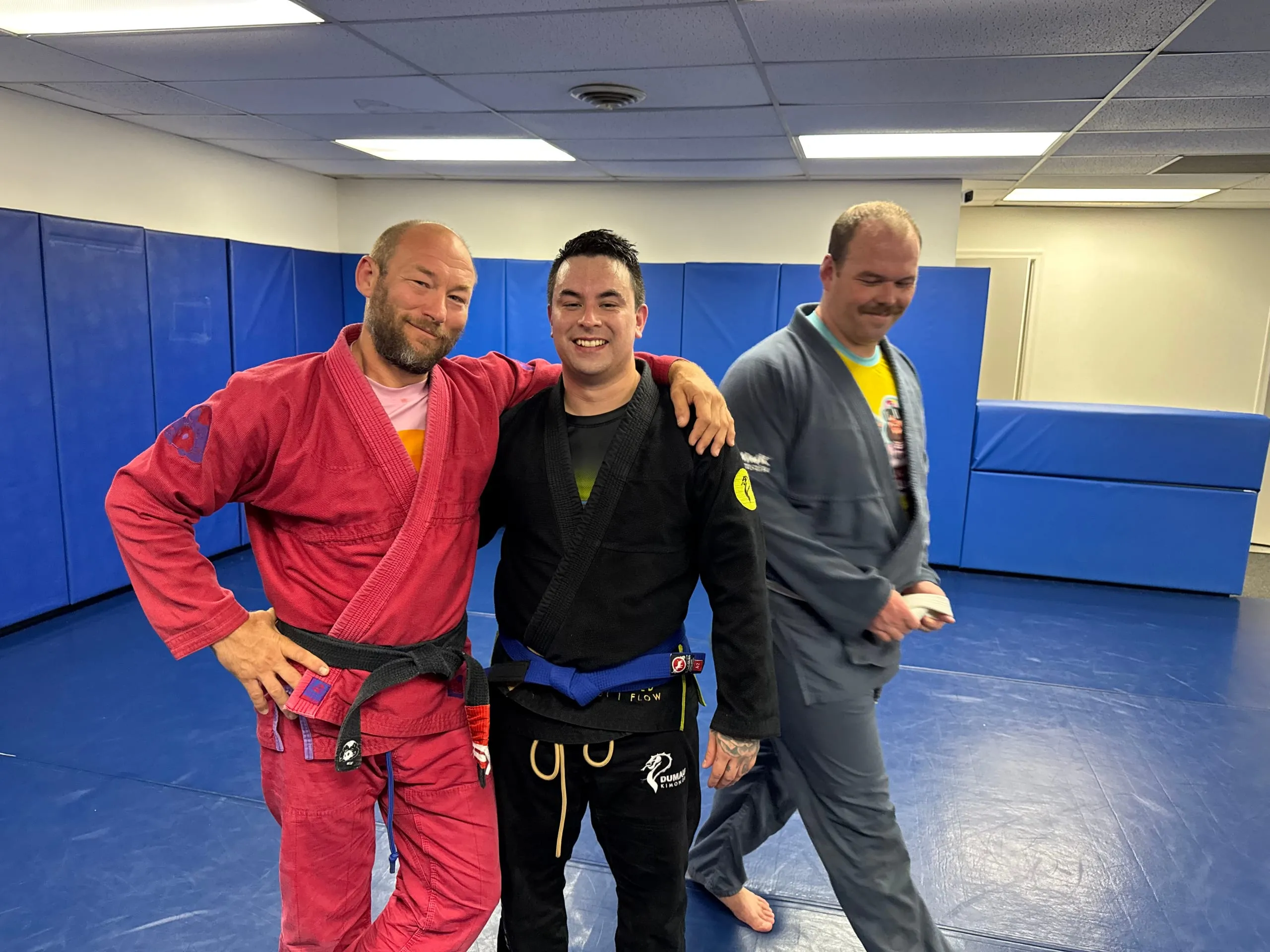 A BJJ instructor congratulates a smiling student wearing his newly earned blue belt.