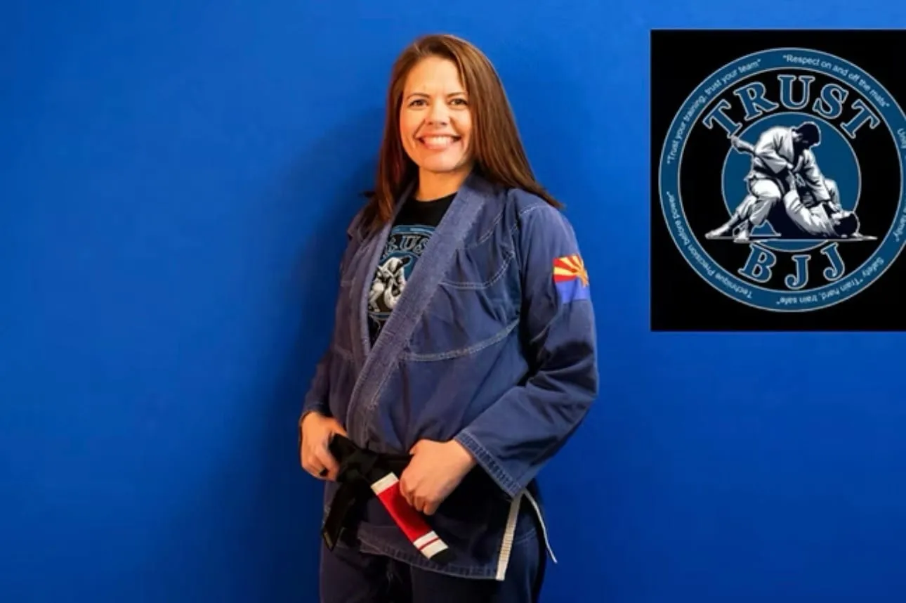 BJJ instructor Missy Baize smiles in a blue gi, holding her black belt.