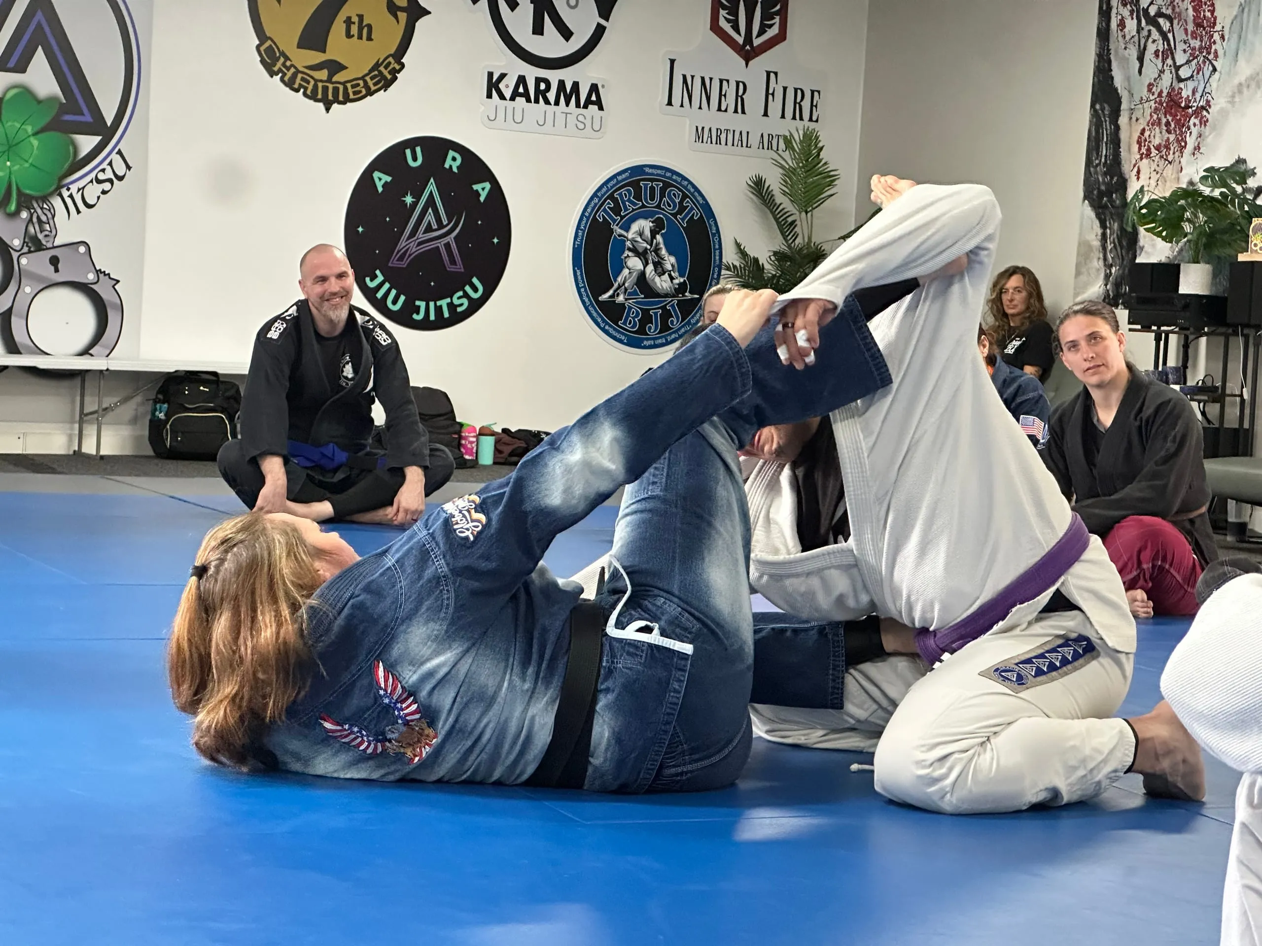 Missy Baize attacks a submission from guard during a Brazilian Jiu Jitsu roll as classmates look on.